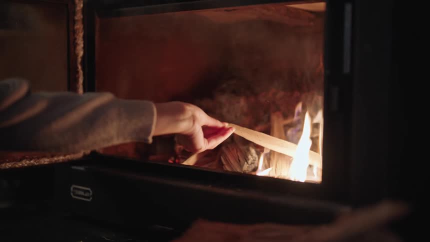 A human hand putting firewood into a fireplace