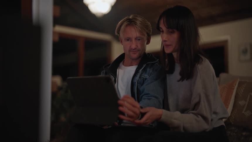 Couple sitting on sofa at home checking something on tablet with keyboard