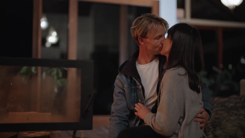 Couple sit together kissing and talking near fireplace
