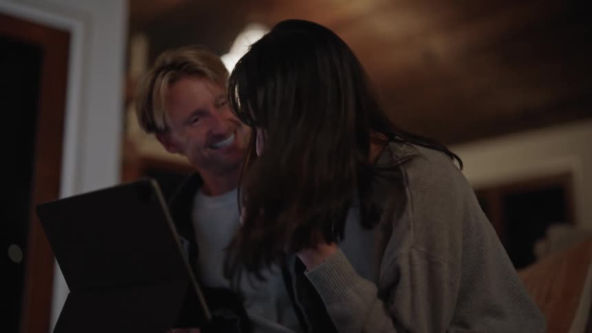 A man and woman talking and smiling while looking at a bright computer screen