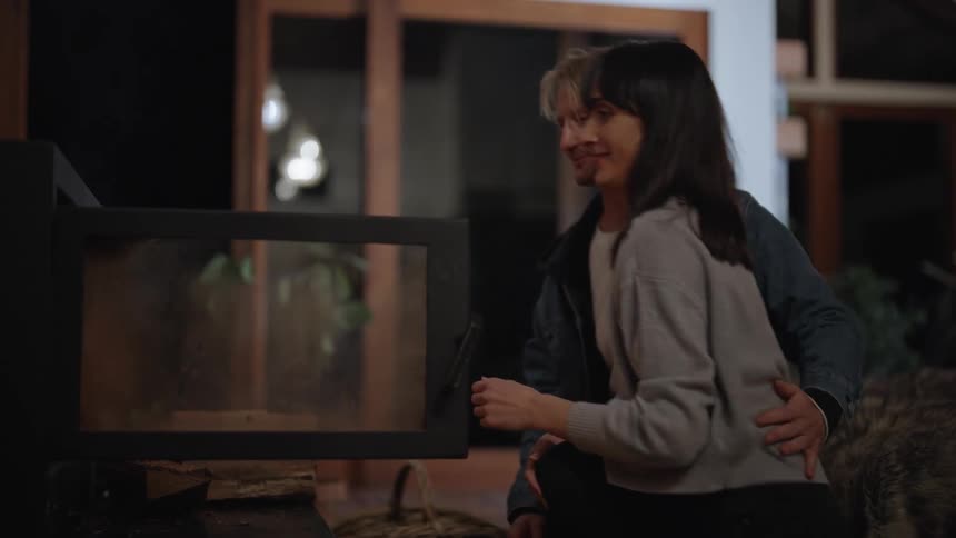 A man and a woman laughing and talking as they add wood to the fire and embrace