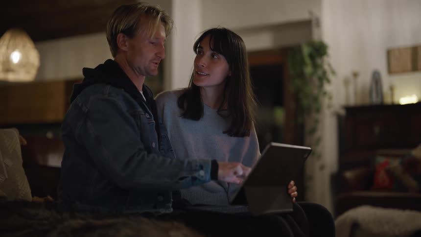 A woman and a man sitting together on a couch discuss what theyre seeing on the laptop the man has in his lap