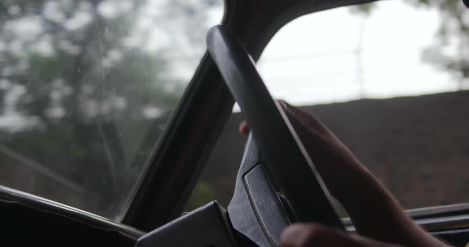 Man with brown shirt holds steering wheel and guides the car through streets