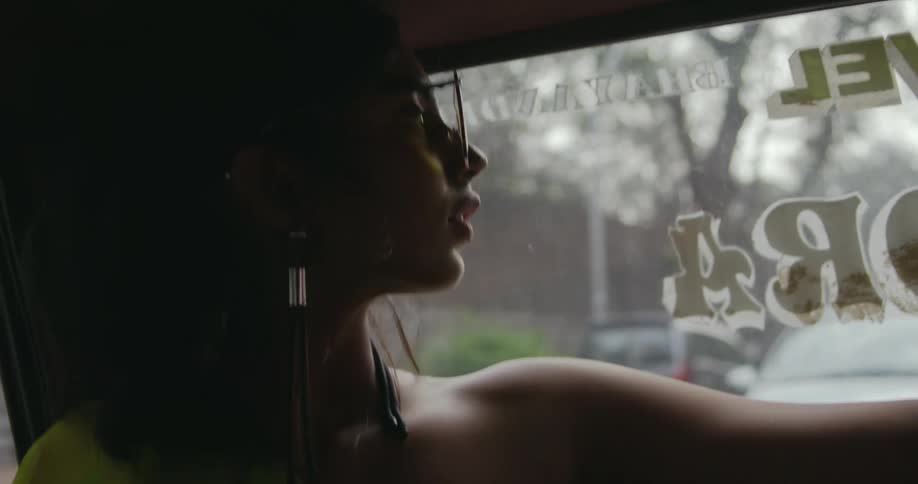 Woman wearing sunglasses sitting inside a moving car looks out of the window