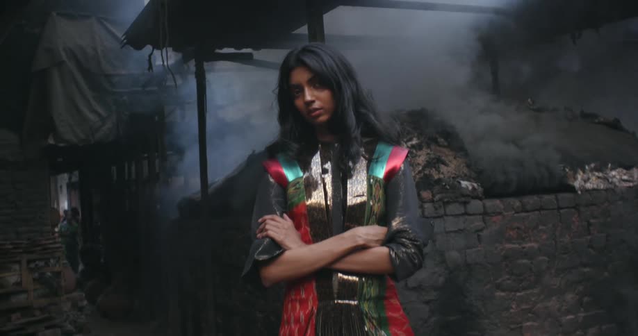 A woman poses in front of a burning building