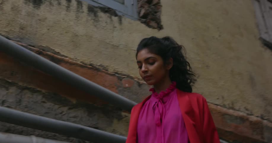 Indian woman with a ponytail and colorful clothes walks down the stairs in an alley and into the streets