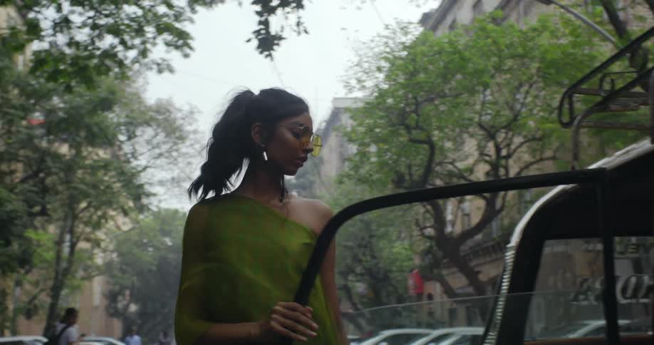 A woman gets out of a black car in the middle of a city road