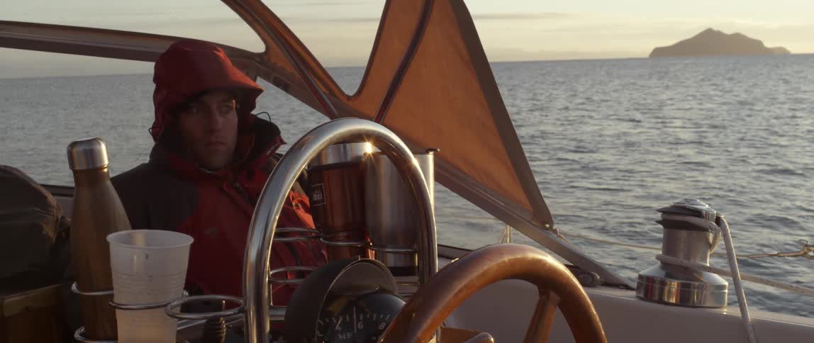 A man is sailing a boat at sunset