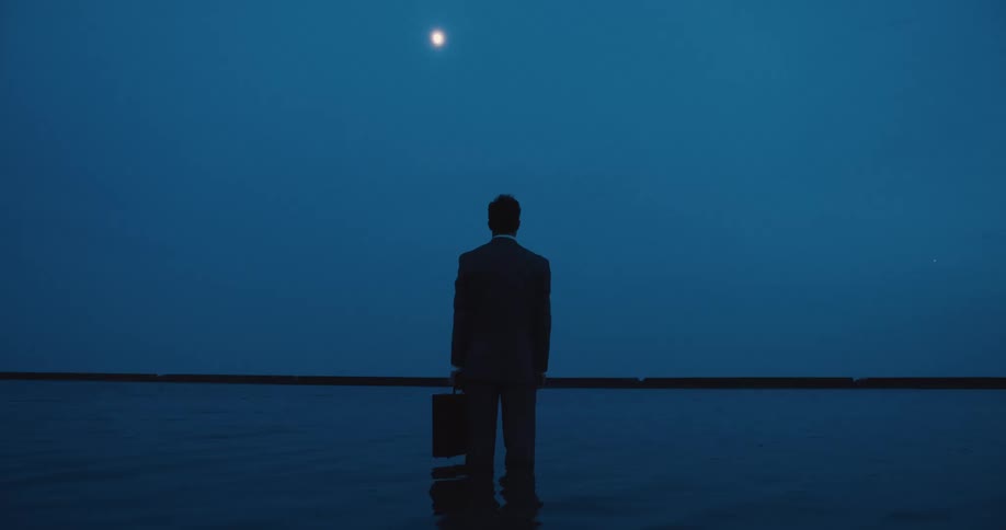 A man in a suit and briefcase and standing in a lake staring straight ahead