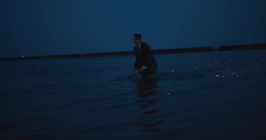 Man wearing business suit staggers while wading out of ocean