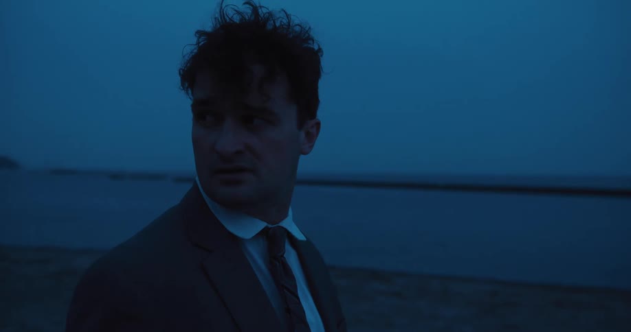 Distraught businessman looks back then runs toward water while carrying briefcase
