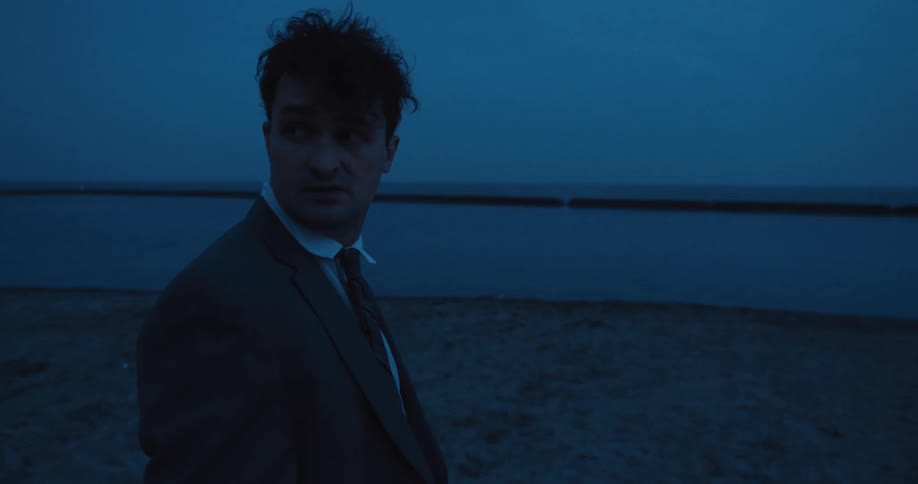 A distraught businessman in a suit runs into the lake at blue hour