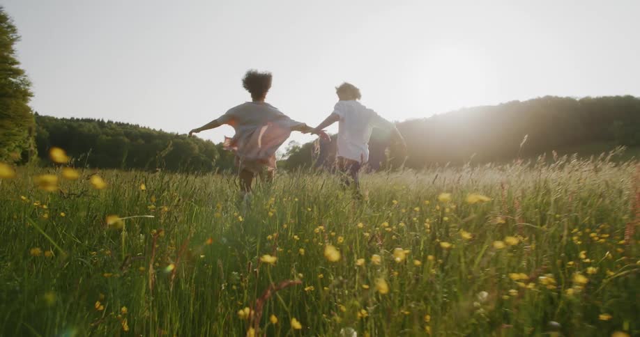 A man and woman run across a field of weeds as the sun in the sky glows everything