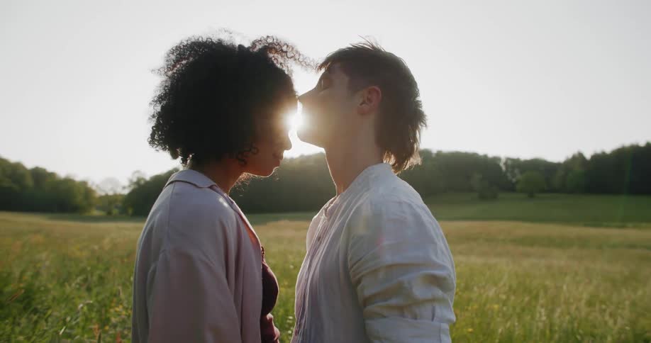 A man leans forward to kiss his female companion on the forehead while standing in a field