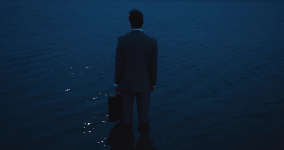 A man wearing a suit and holding a briefcase standing in a lake up to his ankles