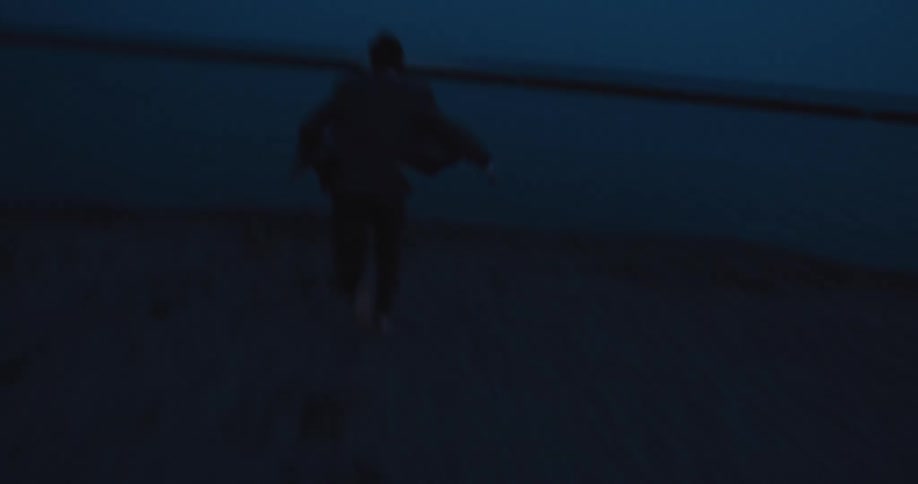 A distraught businessman in a suit runs into the lake at blue hour splashing and sinking