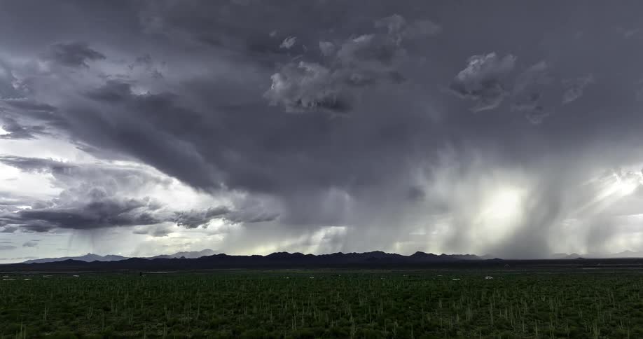 Time lapse of a storm forming over mountains on the horizon as rain pours down with the sun on the horizon