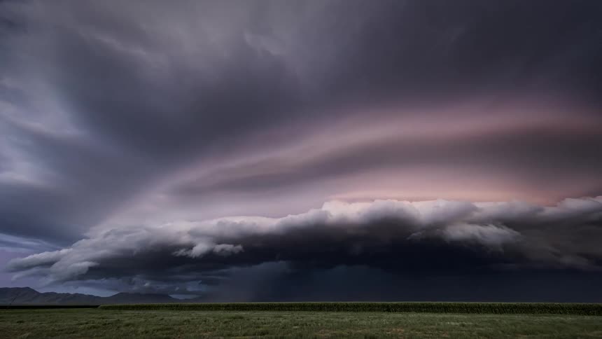 Dark storm clouds flow across grassland as lightning strike on horizon