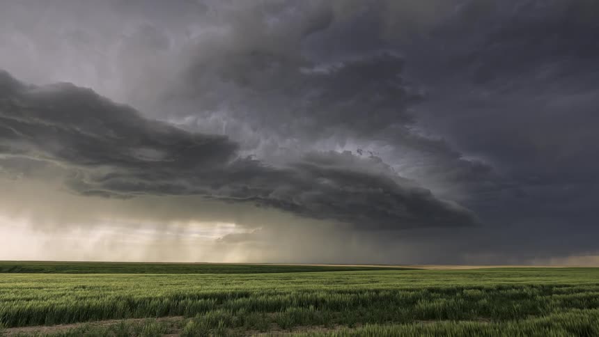 Time lapse of a cloudy storm rolling over the skies across a wide open field as rain pours down