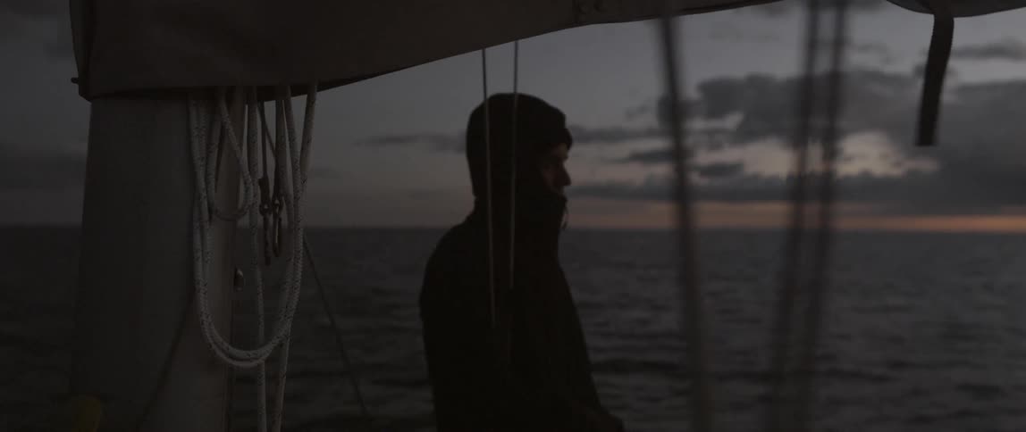 A man is taking in the view off the side of a moving boat at dawn