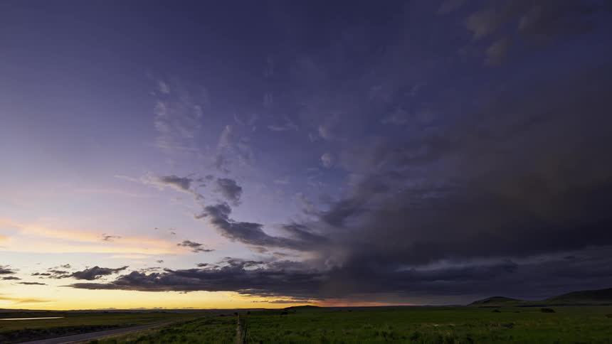 Traffic moves along highway though countryside under storm cloudsat sunset