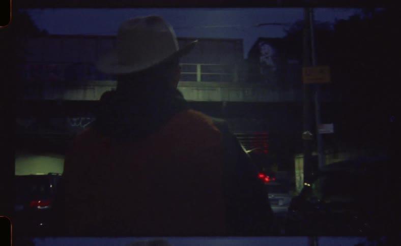 A man wearing a cowboy hat walks down the street at night