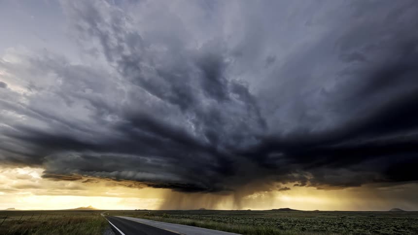 A huge storm cloud moves across the sky quickly over a road
