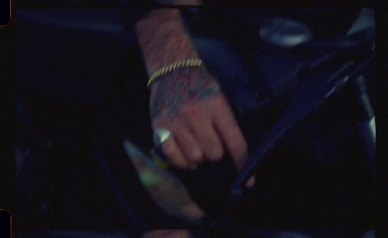 A man with rings and a cowboy hat tries to speed up his motorcycle that is stopped and is checking some parts