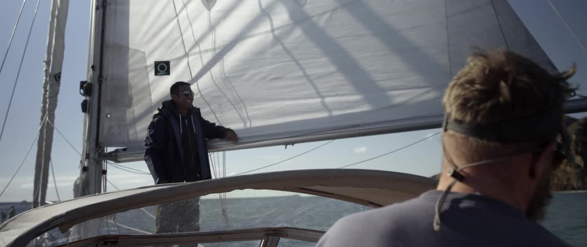 A man is leaning on the sail of a boat talking