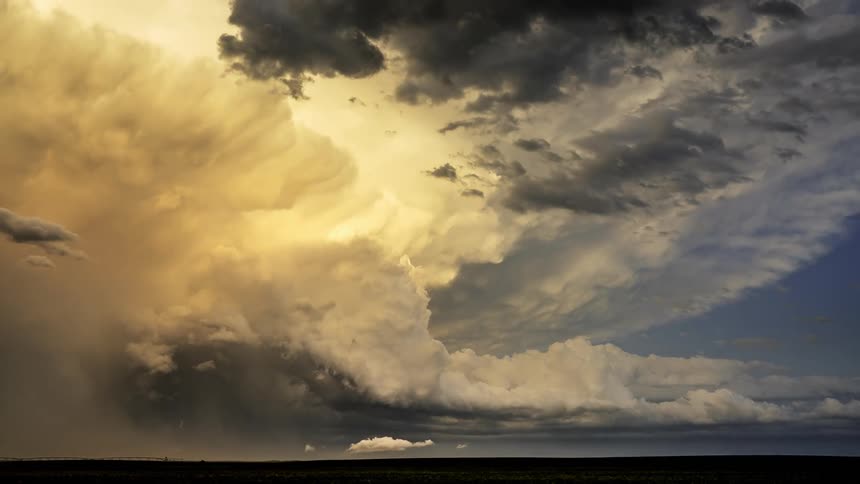 A black cloud heading towards a white cloud that is illuminated with sunlight