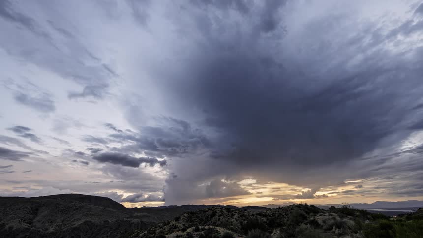 Full clouds pass quickly in the sky and cover the sunset that is setting on the horizon