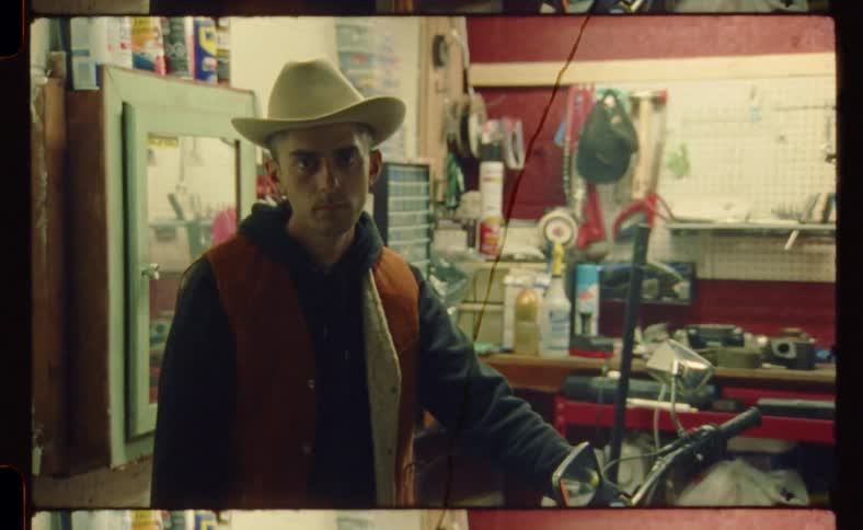 A man in a cowboy hat standing in a garage staring straight ahead