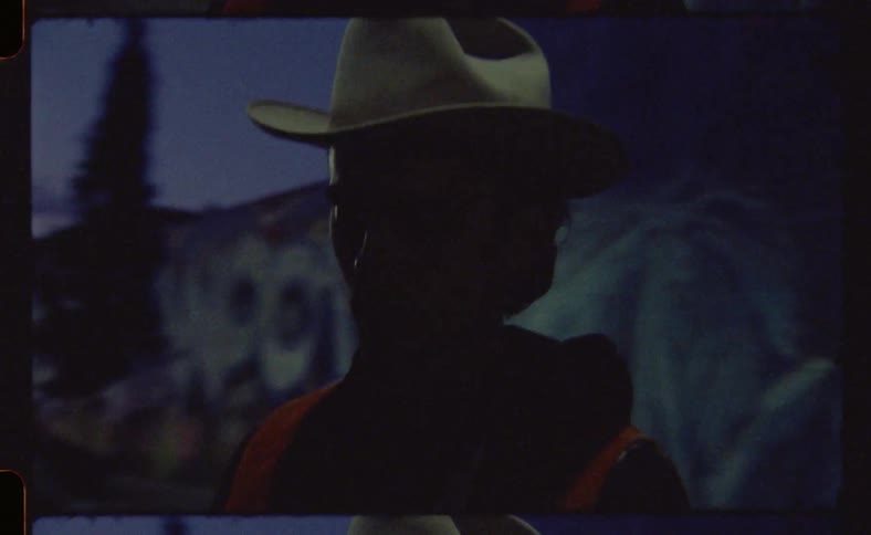 Archival close up of a man wearing a cowboy hat holding an old camera up to his face while taking a picture