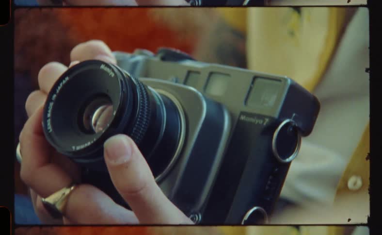 A man wearing a gold ring and a gold wristwatch holding and adjusting a camera lens