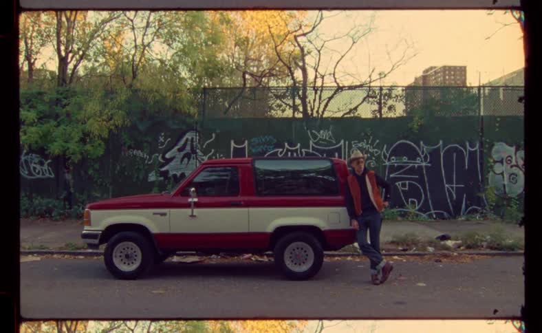 A man leans against a red car in an urban neighborhood