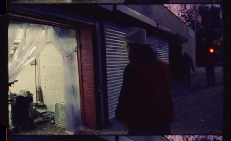 A man with a hat getting out of the car and walking into an interior with a motorbike inside