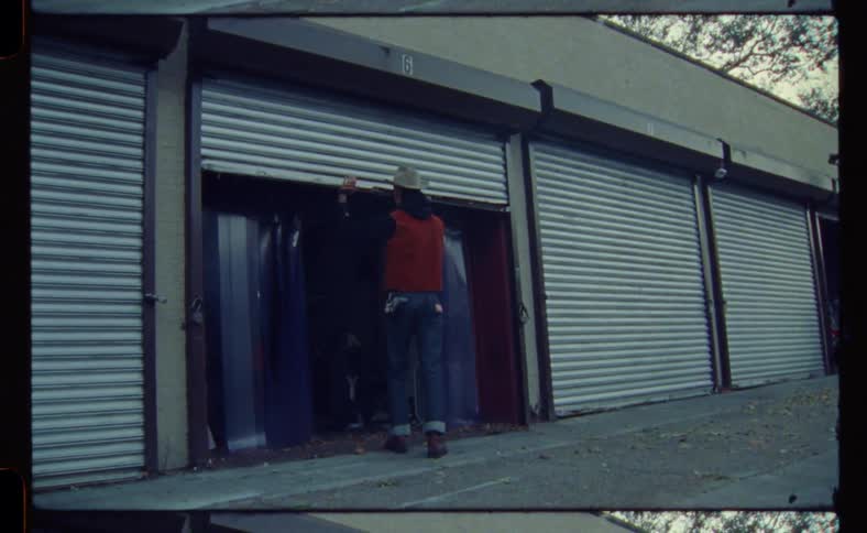 Man wearing a cowboy hat opens the roll up doors of a small storage unit