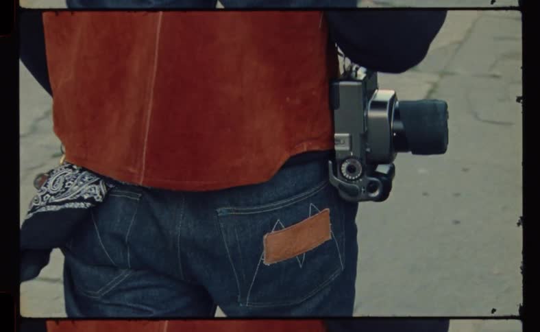 Man wearing leather a vest and jeans carries a camera