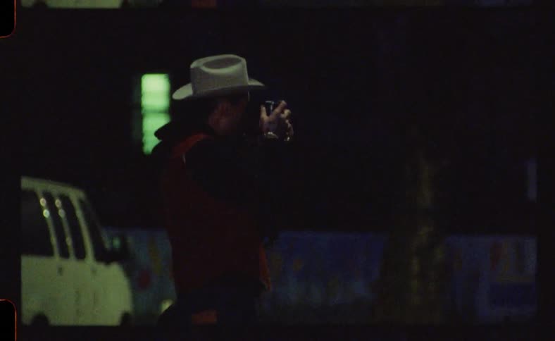 Man wearing a cowboy hat takes pictures on the city streets at night