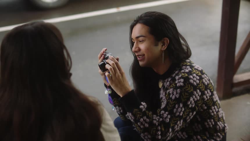 Man with long hair and earrings photographs woman posing and laughing
