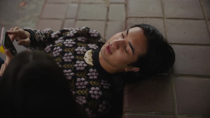 Close up of a young man laying on tile steps while holding his cell phone and talking to someone sitting next to him