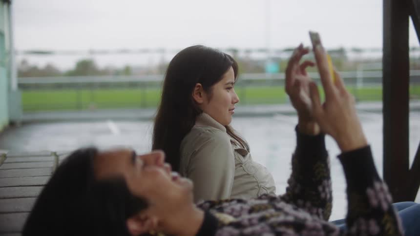 A man talks to a woman while laying down and using a smartphone outdoors