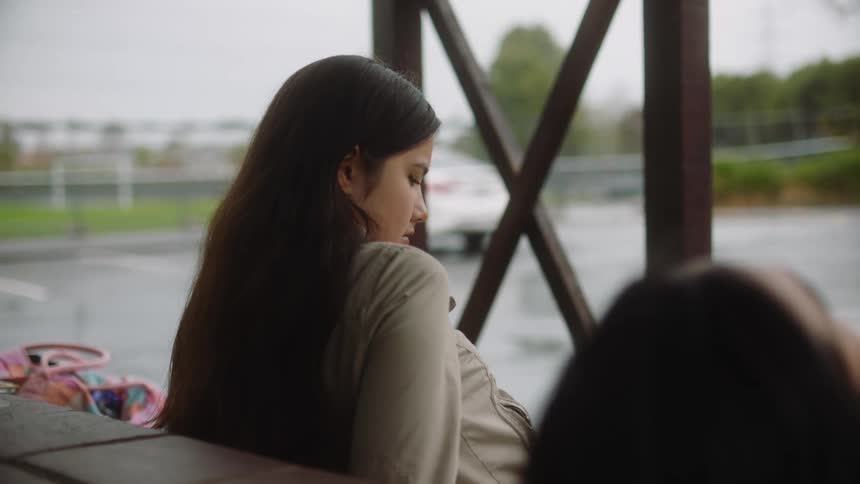 Woman with straight brown hair and gray jacket looks out the windows on a cloudy day