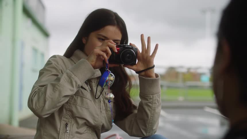 Two young women sitting together taking pictures of each other on a cloudy day