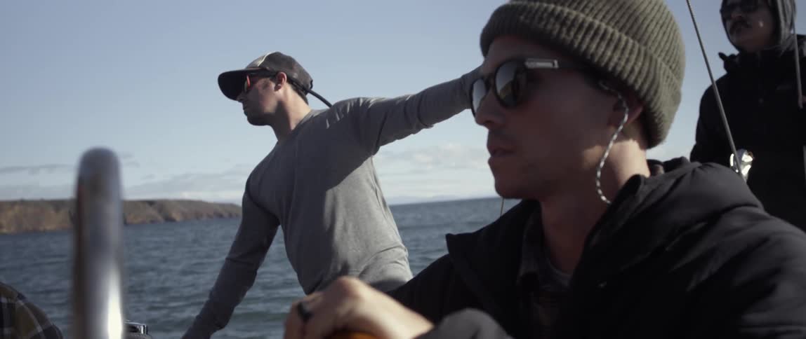 A man is steering a boat while another leans against the railing