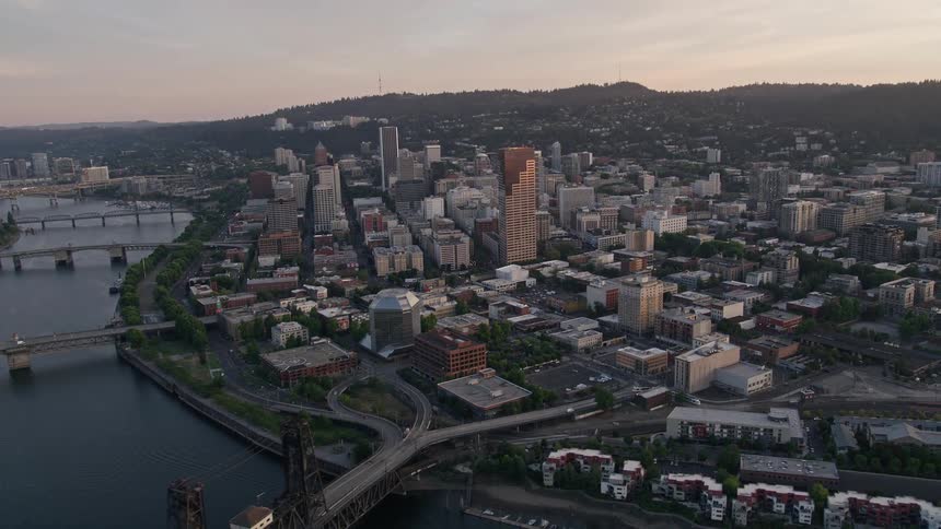 Aerial footage of downtown Portland Oregon at sunset flying over the Willamette River Steel Bridge and high-rise buildings