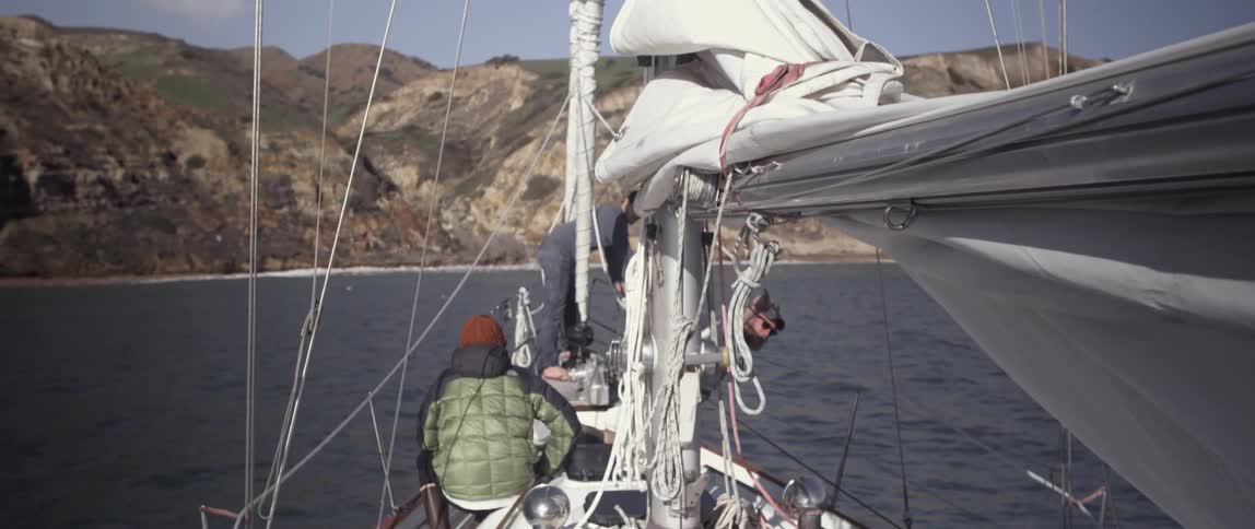 People sit on the edge of a boat with it's sail down