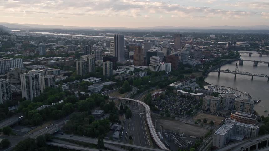 an aerial view of Downtown Portland at sunset approaching and flying over the iconic KOIN Center and Wells Fargo Center buildings amidst a metropolis backdrop