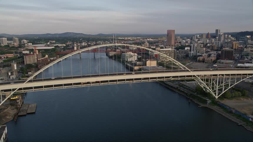 Aerial footage captures a stunning sunset over the Willamette River and Fremont Bridge panning to downtown Portland Oregon showcasing its high rises and bustling city life