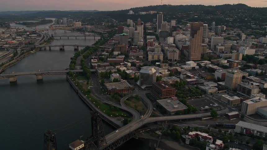 Aerial footage of multiple bridges crossing the Willamette River in downtown Portland during twilight showcasing the high-rise buildings and cityscape